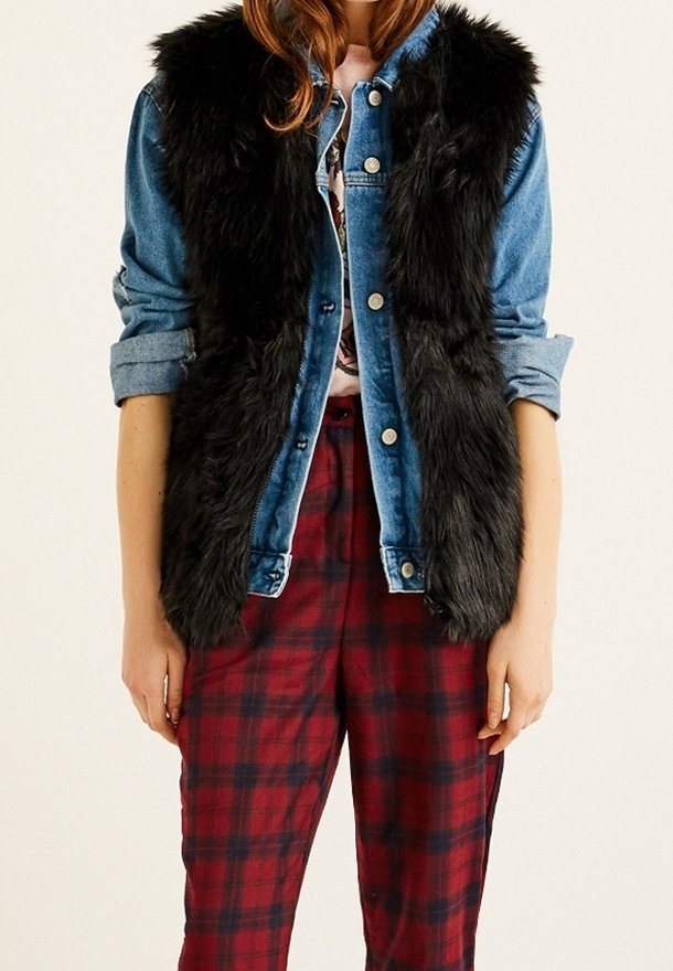Personne portant un gilet en fausse fourrure noire par-dessus une veste en jean bleu avec les manches retroussées et un pantalon à carreaux rouges.