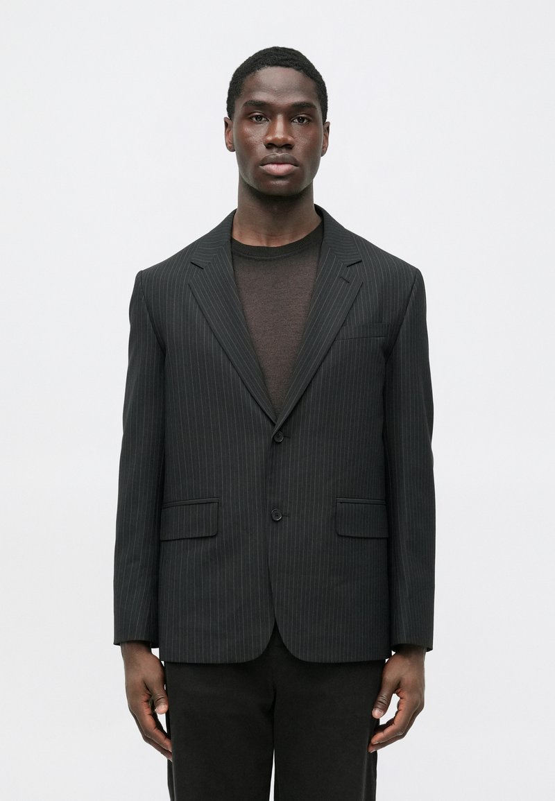 Čierne sako s prúžkami s prispôsobeným strihom, dvoma prednými vreckami a výrezovými klopami, nosené cez tmavý, textúrovaný top.