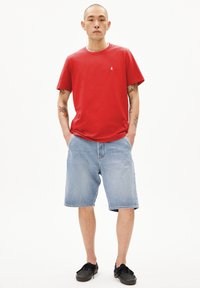 T-shirt en coton rouge à manches courtes et petit logo blanc. Associé à un short en denim bleu clair et des baskets noires.