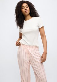 Λευκή ριμπ μπλούζα με κοντά μανίκια και κυματιστές άκρες, συνδυασμένη με ροζ ριγέ πυτζάμες με ελαστική μέση και διακοσμητικά κουμπιά.