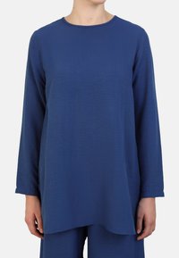 Blue long-sleeve top with a crew neckline, featuring a textured fabric and a relaxed fit, extending slightly longer at the hem.