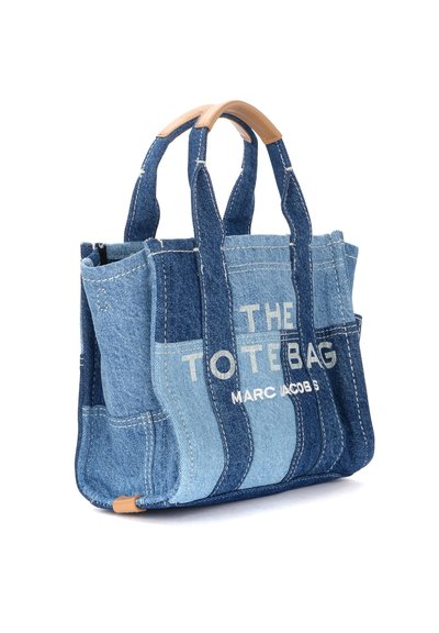 Denim tote bag with varying shades of blue, double handles, and leather accents. Features white printed text for branding.