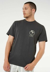 T-shirt in cotone grigio scuro con una piccola immagine di una palma e la scritta "RIP CURL" color crema sul lato sinistro del petto. Design classico con scollo rotondo.