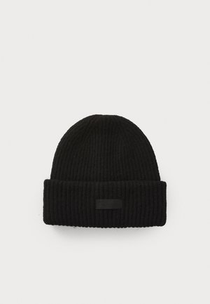 Bonnet en tricot côtelé noir avec un revers retroussé. Présente une petite étiquette noire sur le revers, mettant en avant un matériau texturé et un design à mailles serrées.