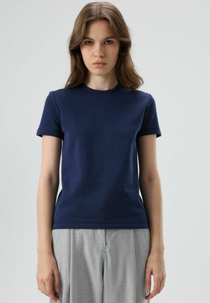 Marineblauw T-shirt met korte mouwen gemaakt van gladde stof; ronde hals, aansluitend model en subtiele rekbaarheid; gecombineerd met lichtgrijze broek.