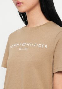 Μπλε βαμβακερό μπλουζάκι κοντό μανίκι με λευκό λογότυπο που γράφει "TOMMY HILFIGER EST. 1985" μπροστά. Λεπτή υφή.