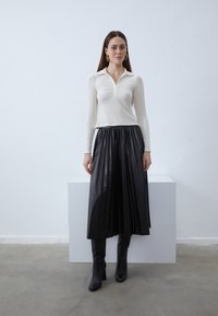White long-sleeve polo shirt with a collar, paired with a black pleated leather skirt and knee-high black heeled boots.