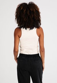 Kerman tank top dengan tali lebar, dipadukan dengan celana hitam berpinggang elastis yang dilengkapi kantong. Kainnya halus dengan sedikit kilau.