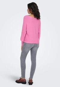 Maglione rosa a coste con vestibilità ampia e scollo ampio, abbinato a jeans skinny grigi e stivali marroni con lacci e suola robusta.