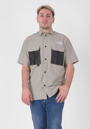 Camicia a maniche corte, grigia chiara, con bottoni, dotata di due tasche in rete nera, logo sul lato sinistro del petto e vestibilità rilassata.