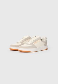 Beige- und cremefarbene Sneakers mit einer strukturierten Oberseite, die ein oranges Logo, weiße Nähte und eine Gummisohle hat.