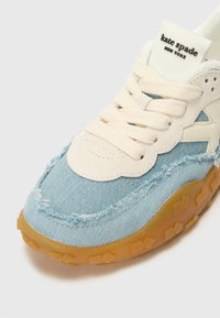 Baskets en denim avec une tige bleu clair, lacets blancs, semelle en caoutchouc texturé et coutures visibles. L'étiquette indique "kate spade NEW YORK."