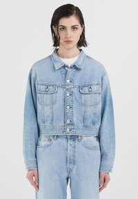 Lyseblå denimjakke med cropped design, med knappelukking, to frontlommer og synlige søm-detaljer.