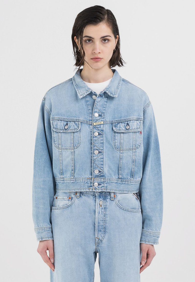 Lyseblå denimjakke med cropped design, med knappelukking, to frontlommer og synlige søm-detaljer.