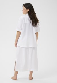 Witte linnen overhemd met korte mouwen en een enkel-lange rok met zijsplitten. Ontspannen pasvorm, minimale naden, gladde textuur en licht materiaal.