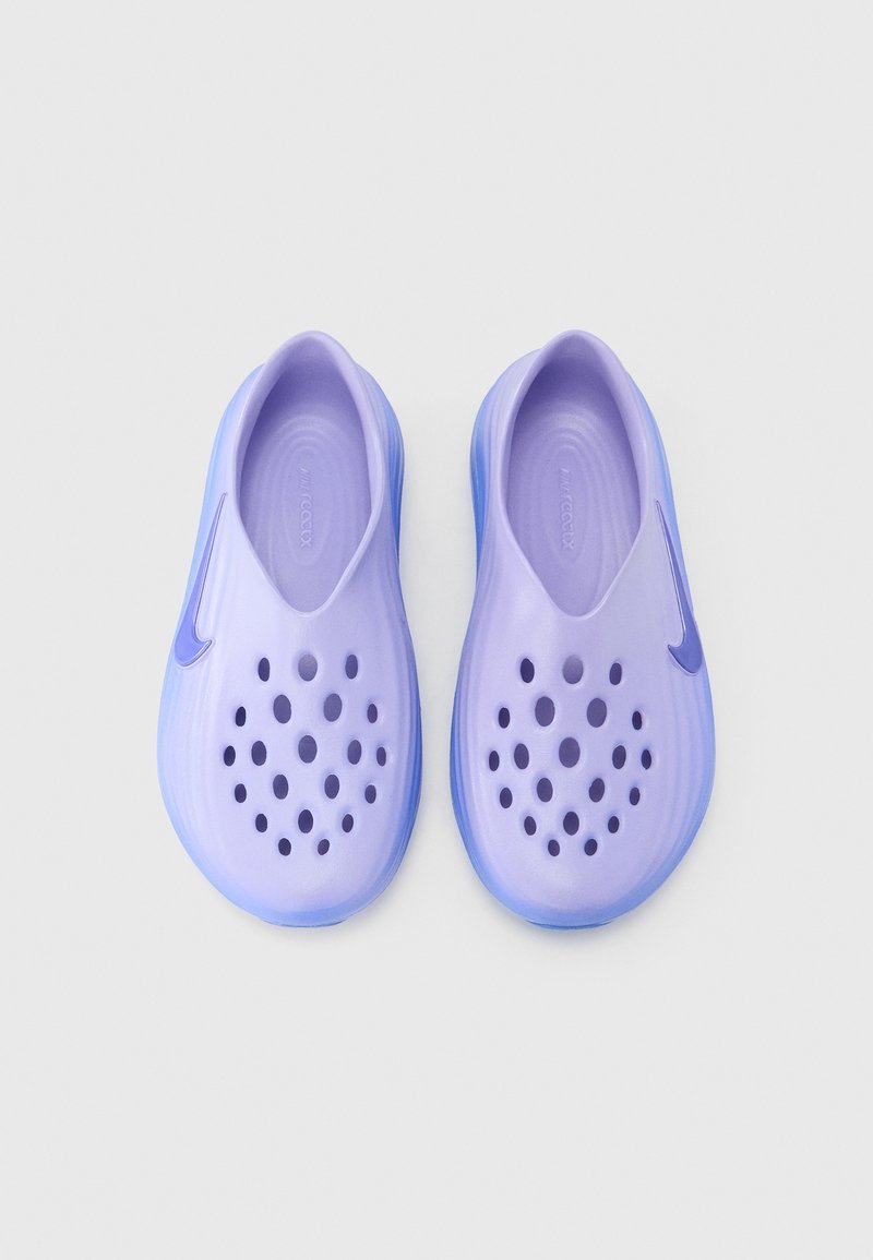 Pair of lavender slip-on foam shoes with circular ventilation holes and Nike swoosh logos on a white background.