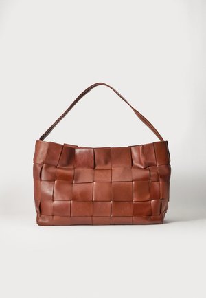 Bolso de cuero marrón con correas anchas tejidas y una sola correa para el hombro sobre un fondo liso y claro.