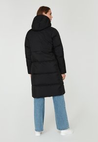 Abrigo acolchado negro con capucha, diseño acolchado y mangas largas, con una cintura ajustada y un corte recto, combinado con jeans de color azul claro.