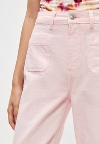 Ανοιχτό ροζ βαμβακερό παντελόνι με ευθεία γραμμή, κλείσιμο με κουμπί μπροστά, δύο πλαϊνές τσέπες και διακριτικές κάθετες ραφές.