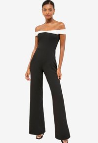 Mono negro con banda blanca sin mangas en los hombros, coupé ajustado y pantalones de pierna ancha. Tela suave con costuras mínimas y silueta elegante.