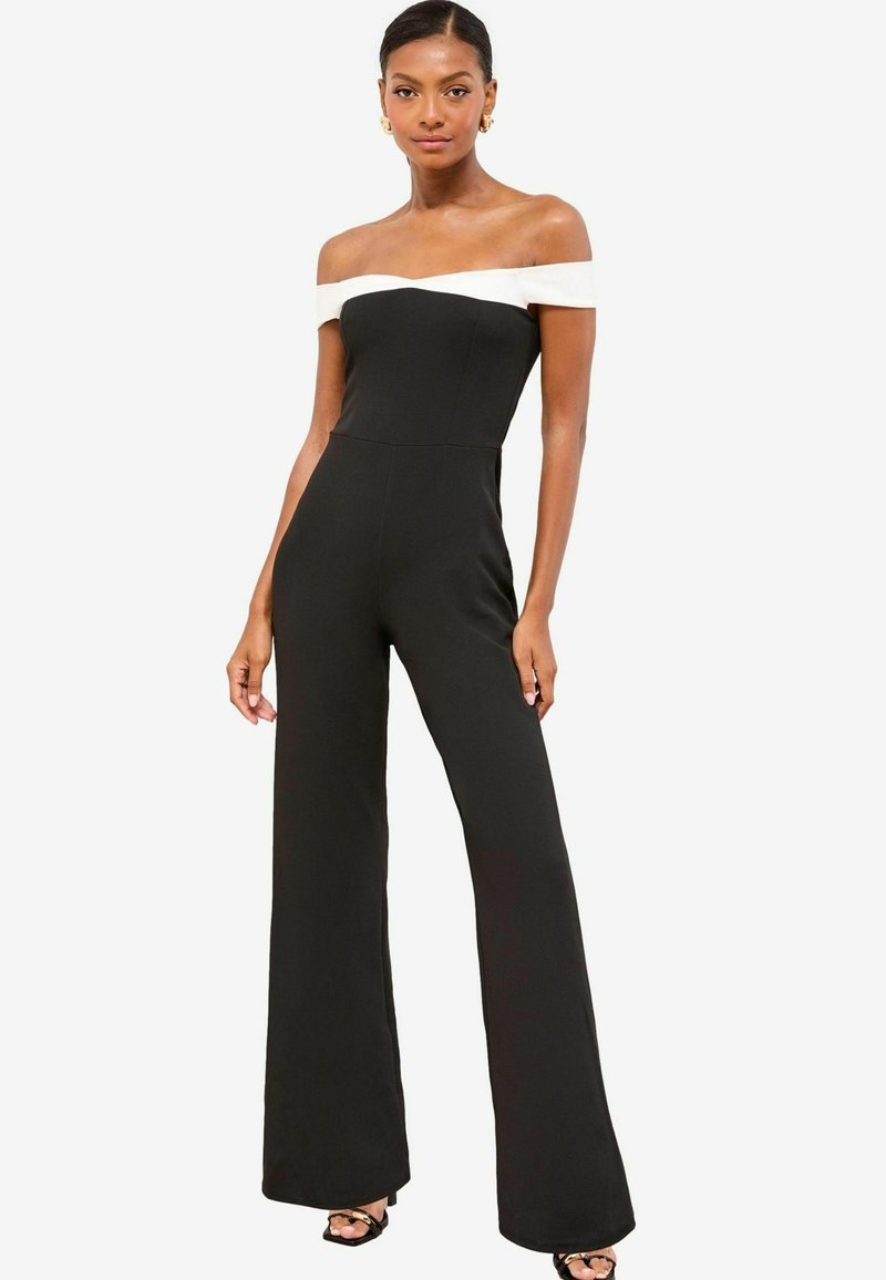 Mono negro con banda blanca sin mangas en los hombros, coupé ajustado y pantalones de pierna ancha. Tela suave con costuras mínimas y silueta elegante.