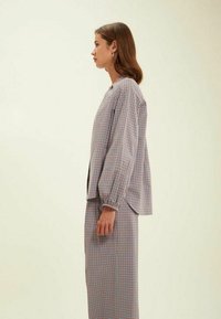 Ensemble blouse et jupe à carreaux en tissu léger. La blouse présente des manches ballons, une coupe décontractée, avec un motif en damier dans des couleurs pastel.