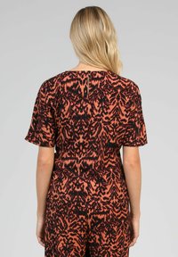 Robe imprimée florale à manches courtes, présentant une palette de couleurs noir et rouille, un tissu texturé et un détail discret d'ouverture dans le dos.