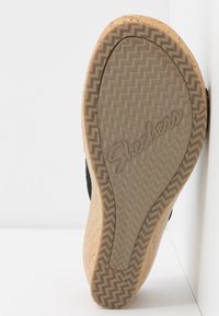 Černá podešev tenisky s vzorovaným gumovým dezénem, vyznačující se logem "Skechers" a texturovaným béžovým okrajem připomínajícím korek.