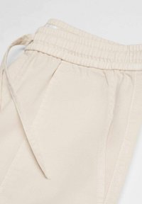 Krémové jogger kalhoty s elastickým pasem, nastavovacím šňůrkovým pasem a bočními kapsami, s hladkou a měkkou texturou látky.