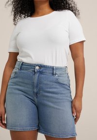 Vit kortärmad skjorta i kombination med ljusblå denimshorts. Shortsen har hög midja, framfickor och en slät yta.