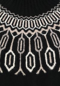 Strickpullover mit schwarzem Grund, der ein geometrisches Muster in Weiß und Hellbraun aufweist. Hoher Kragen und weiche Textur.