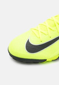 Ljusstark gul fotbollssko med en strukturerad ovandel, svart Nike swoosh-detalj och hexagonal yttersula för grepp. Snören är också gula.