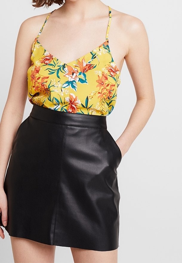Camisole jaune à fleurs avec bretelles fines associée à une mini-jupe en cuir noir taille haute. Le tissu est lisse avec un léger brillant.