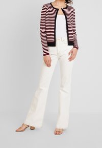 Röd och vit randig cardigan med svart kant, med rund halsringning och fickdetaljer, i kombination med off-white utsvängda jeans och beige klackar.