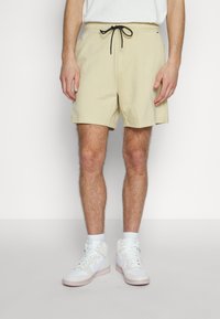 Beige shorts i bomull med elastiskt midjeband, svart snodd och sidofickor. Bärs med vita högstövel sneakers och strumpor.