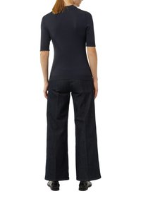 Granatowa bluzka krótko rękawowa o dopasowanym kroju, zestawiona z szerokimi spodniami z ciemnego dżinsu. Materiały wydają się gładkie i teksturowane.