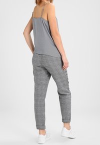 Top grigio senza maniche con spalline sottili abbinato a pantaloni tapered grigi e neri a scacchi, completato da sneakers bianche.