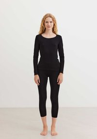 Fekete, hosszú ujjú blúz, hullámos nyakkivágással, fekete, testhezálló leggings-szel párosítva. Mindkettő sima textúrájú és szoros illeszkedésű.