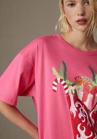 Lyserød kortærmet t-shirt med et farverigt ferie-tema grafisk design med peberkager, slikstokke og festlige elementer.
