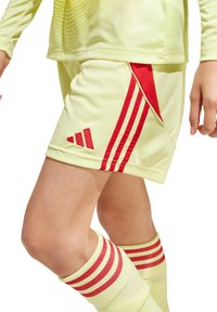 Lichtgele voetbalshorts met rode verticale strepen en het Adidas-logo. Zachte stof met een atletische pasvorm, gecombineerd met bijpassende sokken met rode strepen.