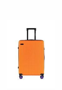 Pomarańczowa walizka twarda z pionowymi rowkami, wysuwanym czarnym uchwytem oraz czterema fioletowymi kółkami dla łatwego przemieszczania.