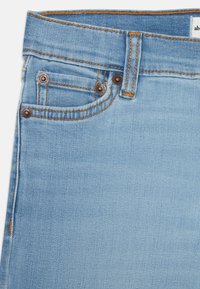 Jasnoniebieskie dżinsy o wysokim stanie, z mosiężnymi guzikami, kontrastowym przeszyciem i małym detalem w postaci kieszonki z przodu.