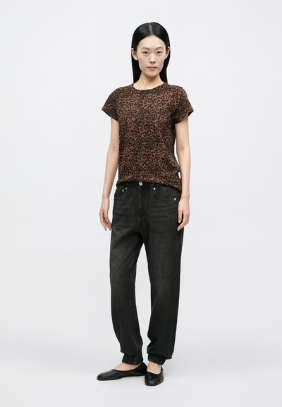 Brązowa bluzka w cętki lamparta z krótkim rękawem i okrągłym dekoltem, zestawiona z czarnymi zwężanymi dżinsami jogger i czarnymi butami wsuwanymi.