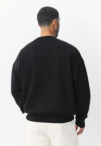 Fekete, túlméretezett pulóver, egyszerű környakú kivitelben, bordázott mandzsettákkal és szegéllyel, puha, matt textúrájú anyagból készült.