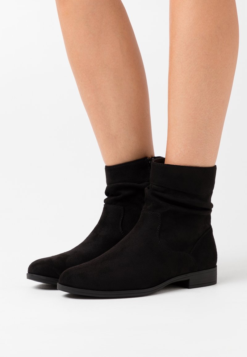 Botines de ante negro con un diseño arrugado, suela plana y punta redonda. Cuenta con una cremallera lateral para poner y quitar fácilmente y una textura suave.