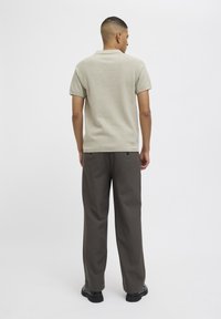 Lys beige kortermet polo skjorte med teksturert strikk, kombinert med mørkegrå løse bukser. Svart fottøy synlig.