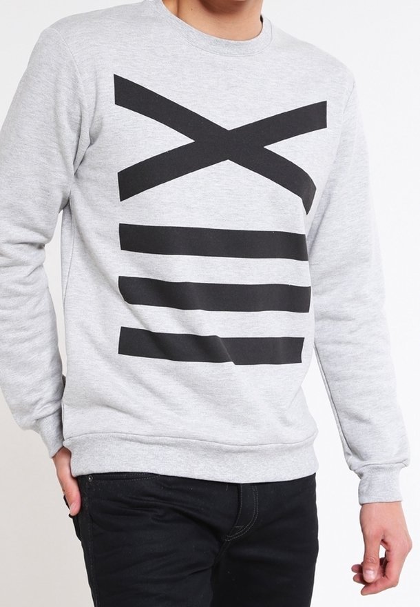 Personne portant un sweat-shirt gris clair avec le chiffre romain XIII en noir gras imprimé sur le devant, associé à un pantalon noir.