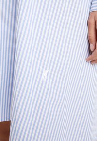 Světle modrá a bílá pruhovaná tkanina s hladkou texturou, na pravém dolním rohu s malým bílým vyšitím.