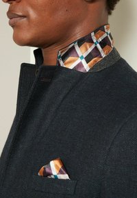 Donkerblauwe textuurjack met een patroonkraag in oranje, paars en turquoise. Inclusief een bijpassende pochet.