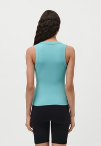 En lys blå, ermeløs topp med en tettsittende design og ribbestrikket tekstur, kombinert med svarte shorts. Ingen synlige mønstre eller beslag.